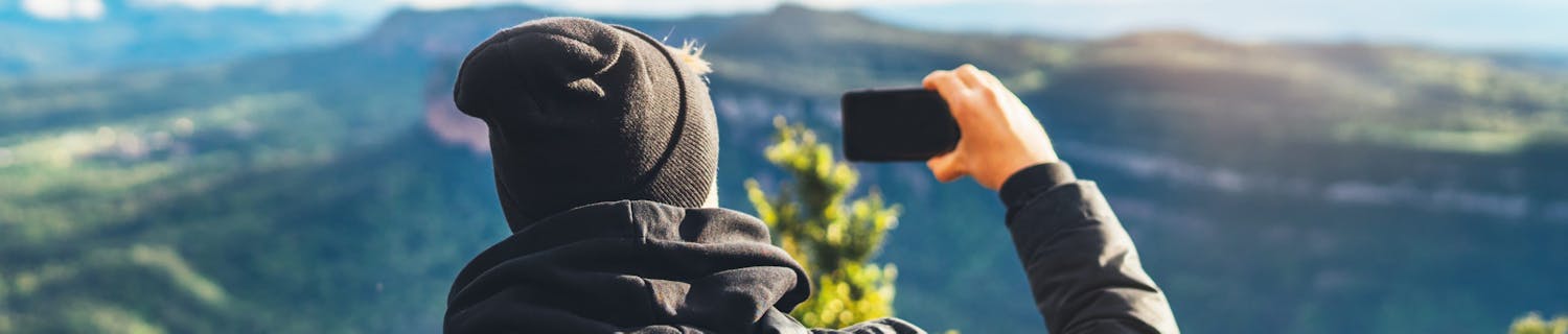 Man sitter i utestol och fotograferar med mobilen